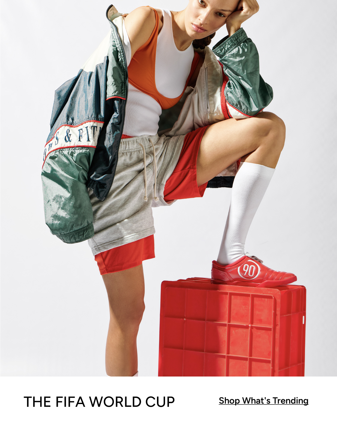 The FIFA World Cup — woman in Nike sportswear and red #90 sneakers posing on a red crate. Shop What's Trending