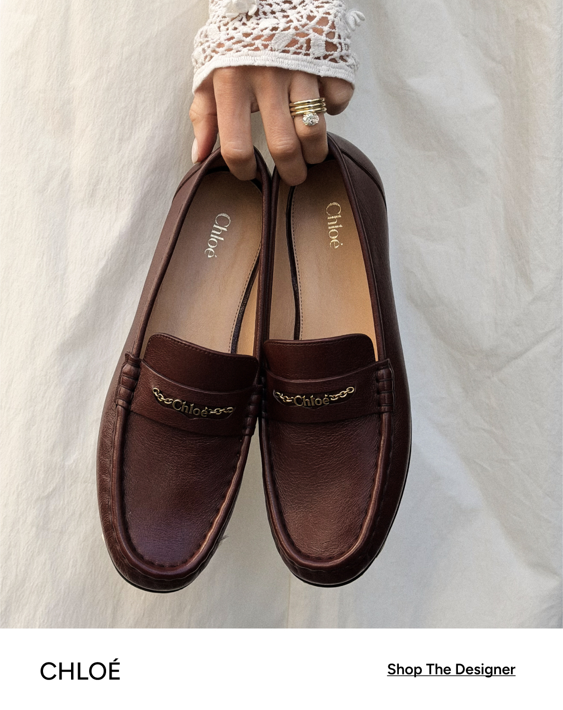 Chloé dark brown leather loafers with gold chain logo detail, held by a ringed hand — Shop The Designer